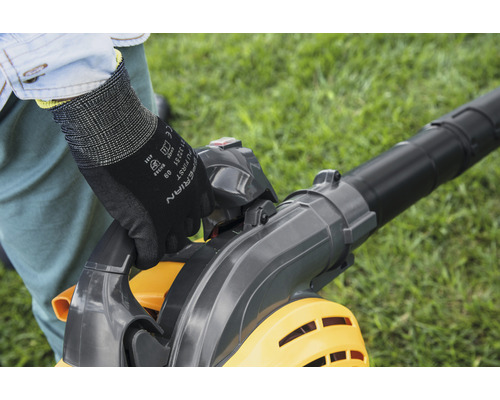 Osoba obsluhuje vysávač lístia v záhrade a má na sebe rukavice.