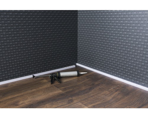 Rohová oblasť miestnosti s podlahovými lištami a pištoľou na kartuše na drevenej podlahe