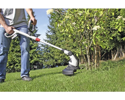 Osoba používa akumulátorový vyžínač na záhrade na kosenie trávy pod kríkom.