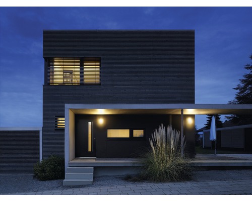 Moderný dom s drevenou fasádou, prístreškom pre auto a osvetlením za súmraku.