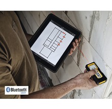 Osoba meria stenu laserovým diaľkomerom a zároveň sa pozerá na tablet s pôdorysom.