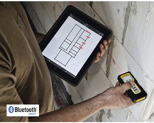 Osoba meria stenu laserovým diaľkomerom a zároveň sa pozerá na tablet s pôdorysom.
