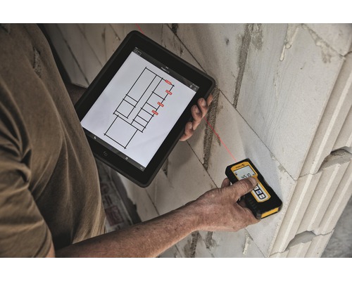 Osoba meria stenu pomocou laserového diaľkomeru a tabletu s plánom budovy