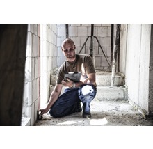 Muž používa laserový diaľkomer na stenu v hrubej stavbe.