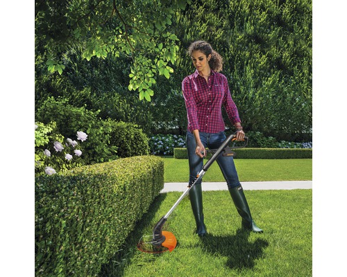 Žena strihá živý plot s vyžínačom trávy v záhrade.