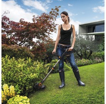 Žena používa vyžínač na trávu v záhrade.