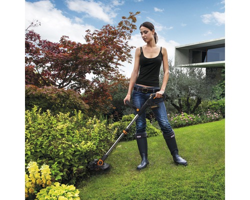 Žena pracuje so sekačkou na trávu v záhrade.