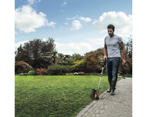 Muž používa v záhrade nožnice na trávu na zastrihávanie okrajov trávnika.