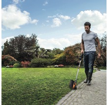 Muž používa vyžínač trávnika na upravenom trávniku.