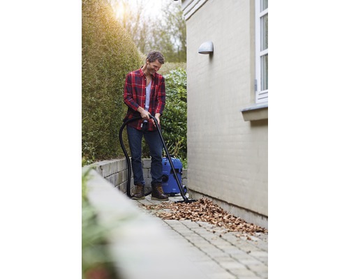 Muž upratuje mokrým a suchým vysávačom lístie z dláždenej cesty.