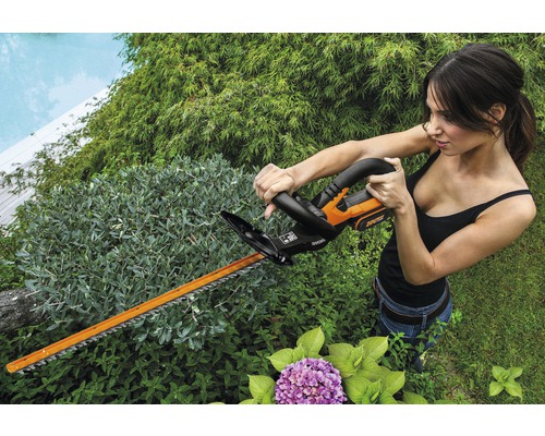 Žena strihá živý plot akumulátorovými nožnicami na živý plot v záhrade