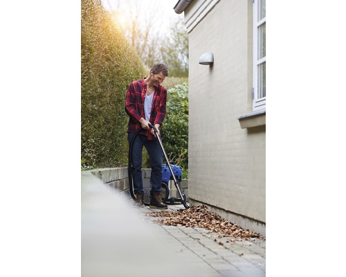 Muž vysáva lístie mokro suchým vysávačom v záhrade.