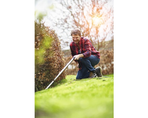 Muž kľačí v záhrade a reže okraje trávnika zastrihávačom okrajov.