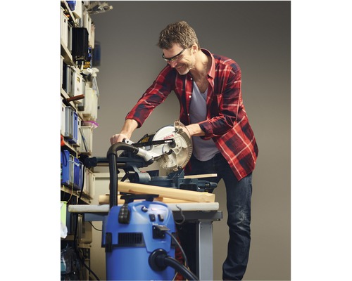 Muž reže drevo pokosovou pílou v dielni. Vedľa stojí vysávač.