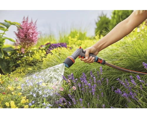 Osoba zavlažuje záhradu záhradnou striekacou pištoľou Gardena.