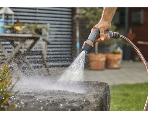 Osoba zavlažuje kameň záhradnou sprchou a záhradnou hadicou.