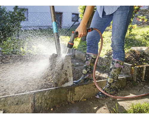 Osoba čistí záhradnú lopatu záhradnou hadicou.