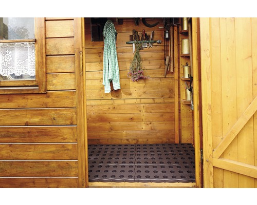 Vnútorný pohľad na drevený záhradný domček s gumovými rohožami na podlahe a rôznym záhradným náradím na stenách