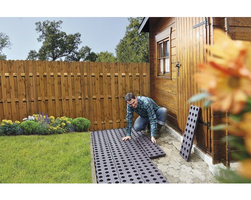 Muž kladie zatrávňovacie dlaždice v záhrade blízko drevenej kôlne a dreveného plota