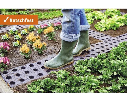 Osoba v gumákoch kráča po záhradnom chodníku medzi rastlinami a kvetmi. Protišmykové.