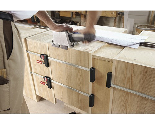 Remeselník pracuje s lamelovacou frézou na drevenom nábytku upevnenom svorkami.