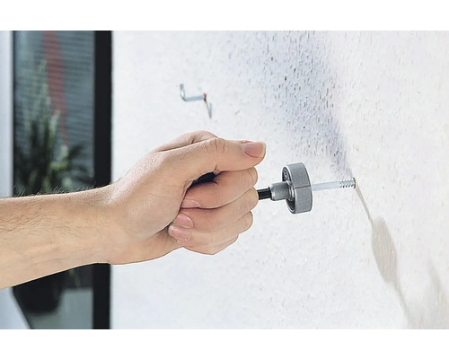 Osoba pripevňuje hmoždinku k stene montážnym nástrojom