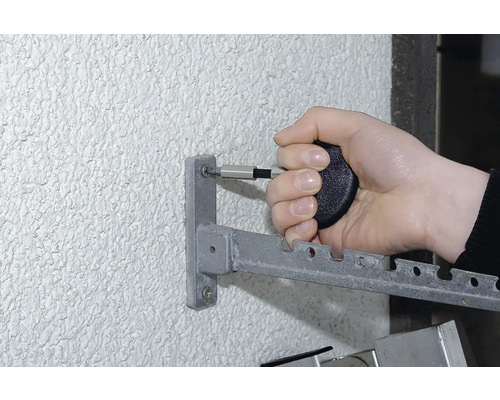 Osoba pripevňuje kovový sušiak na bielizeň ku stene pomocou skrutkovača.