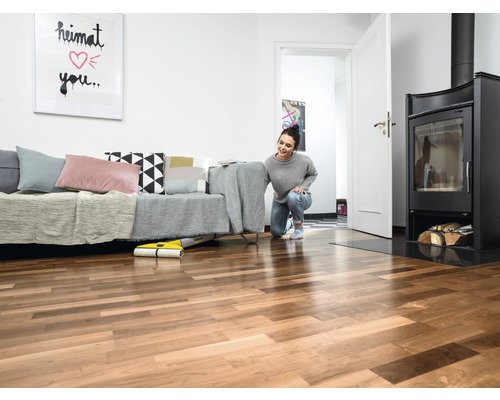 Žena používa žltý mopovací robot v obývacej izbe s pohovkou, krbom a drevenou podlahou.