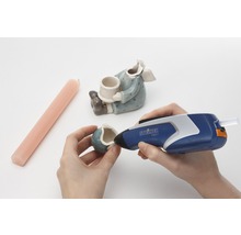 Osoba opravuje keramickú figúrku horúcou lepiacou pištoľou