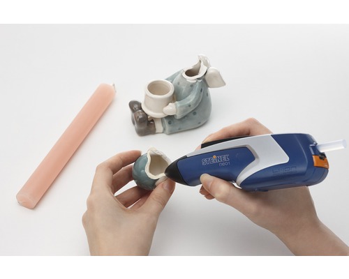 Osoba opravuje keramickú figúrku horúcou lepiacou pištoľou