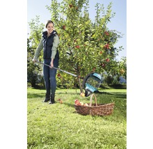 Žena zbiera jablká pomocou zberača ovocia a košíka v záhrade.