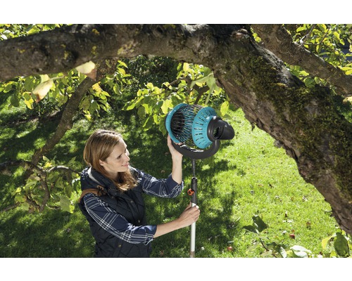 Žena používa zberač ovocia v záhrade pod stromom.