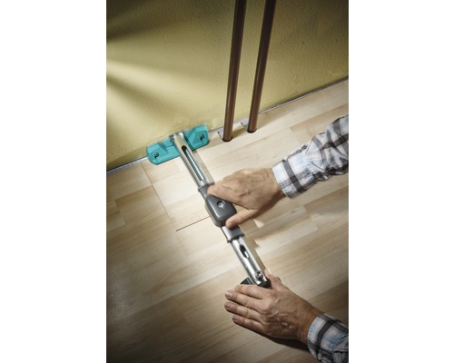 Osoba pokladá laminát pomocou sťahováka pozdĺž steny.