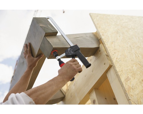 Osoba upevňuje drevené trámy k drevenému rámu pomocou svorky.