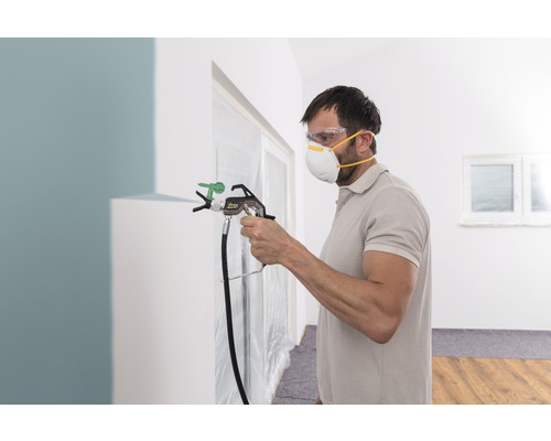 Muž používa striekaciu pištoľ na farbu v interiéri