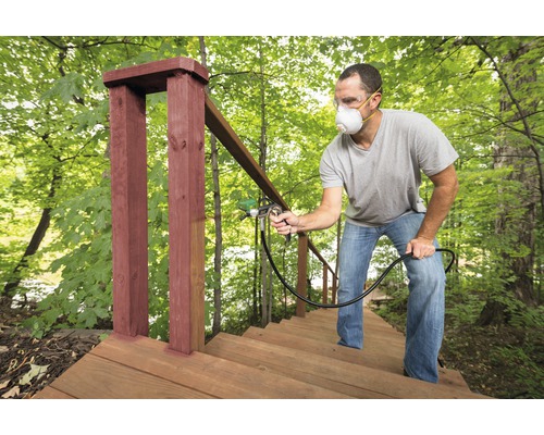 Muž natiera drevené vonkajšie schodisko striekacou pištoľou