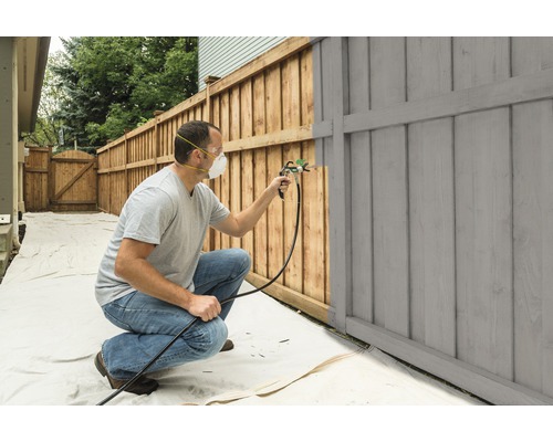 Osoba natiera drevený plot striekacou pištoľou.