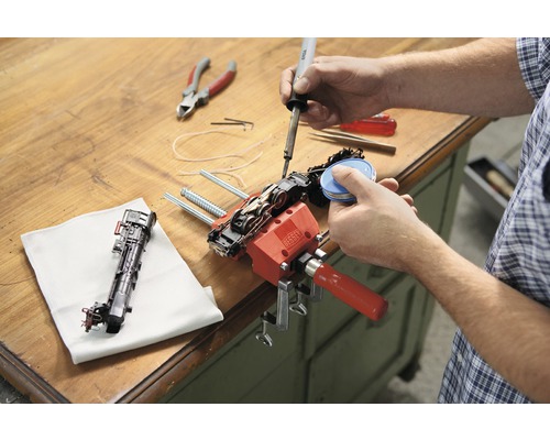 Osoba opravuje model železnice pomocou spájkovačky a skrutkovej svorky