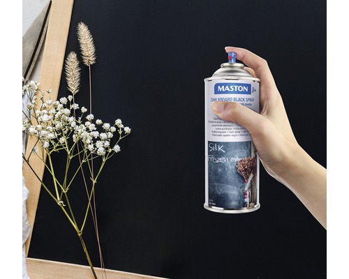 Ruka drží sprej Maston tabuľová farba čierna pred tabuľou.