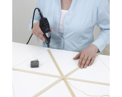 Osoba vŕta otvor do drevenej tyče pomocou multifunkčného nástroja Dremel.