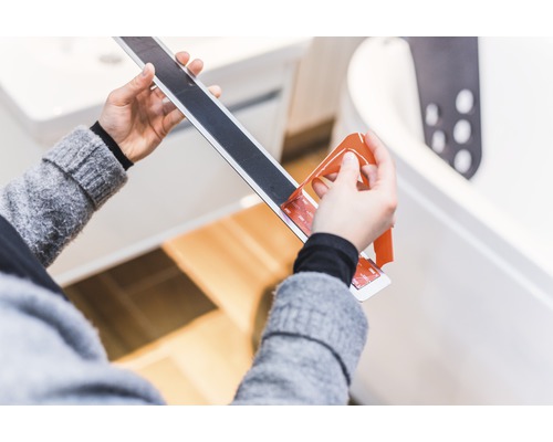 Osoba odstraňuje ochrannú fóliu z protišmykového pásu