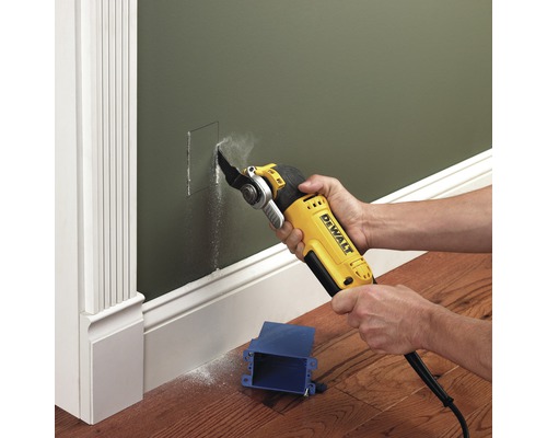 Oscilačné elektrické náradie vyrezáva otvor do zelenej steny pre modrú spojovaciu krabicu.