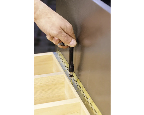 Ruka skrutkuje pánt na drevenú konštrukciu pomocou skrutkovača