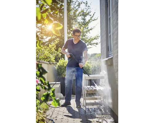 Osoba čistí záhradnú lavicu vysokotlakovým čističom vonku.