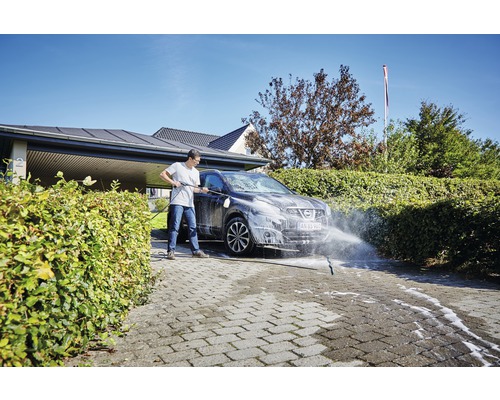 Osoba čistí auto vysokotlakovým čističom na dláždenej príjazdovej ceste