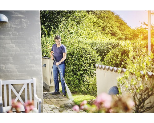 Muž čistí terasu tlakovou umývačkou v záhrade.