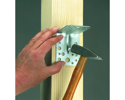 Rohový konektor je kladivom pripevnený k drevenému trámu.