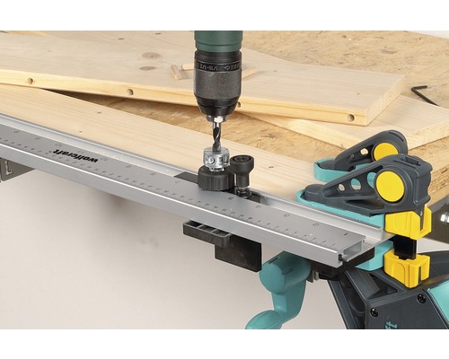 Vŕtačka s vŕtacím puzdrom pre hmoždinky vŕta do drevenej dosky pomocou hmoždinkových svoriek Wolfcraft.