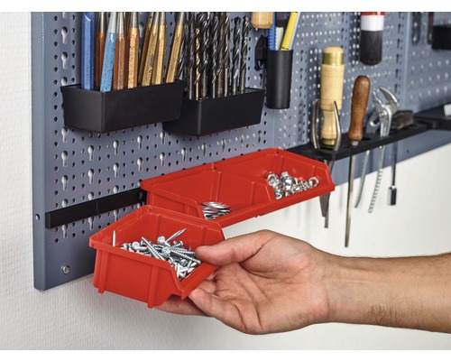 Dierkovaná stena na náradie s rôznym náradím a červenými úložnými boxami