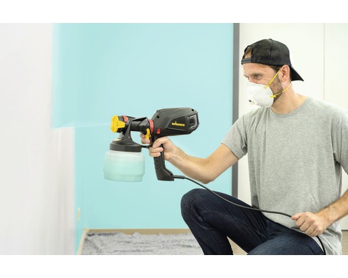 Muž používa striekaciu pištoľ Wagner na natieranie steny.